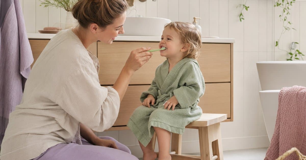 Forelder hjelper baby med å pusse tennene i lyst baderom med trygg fluortannkrem