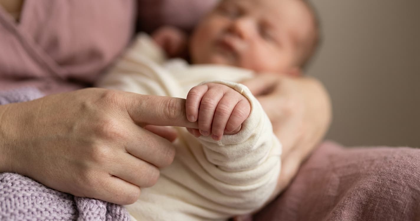 Nyfødt baby griper rundt morens finger med liten hånd
