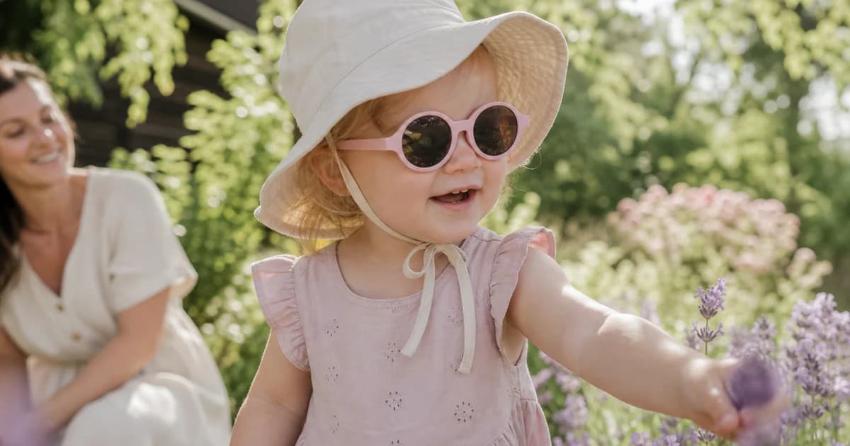 Småbarn med solbriller og solhatt leker i hagen på en lys norsk sommerdag