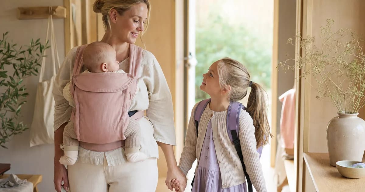 Forelder med baby i bæresele som følger storesøsken til skolen