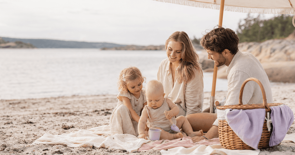 Foreldre med baby under parasoll på en norsk sandstrand en solrik sommerdag