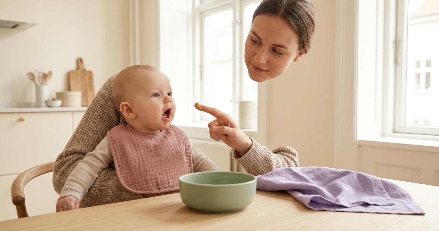 Mor gir baby på 5 måneder liten smaksprøve av peanøttpuré med finger